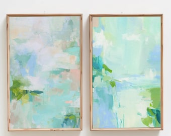 May include: Two rectangular wall art pieces in light wooden frames featuring abstract paintings. The artwork displays blended brushstrokes of mint green, soft blue, white, and pale peach tones, creating a layered, fluid composition across both canvases.
