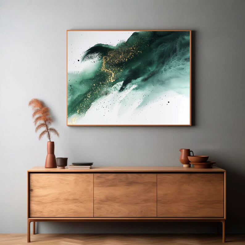 May include: A framed abstract painting with a green and gold color scheme. The painting is on a white background and features a large, abstract shape in shades of green with gold flecks. The painting is hanging on a gray wall above a wooden cabinet.