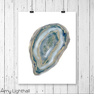 May include: A watercolor print of a geode slice, featuring shades of blue, gray, and gold. The artwork is displayed on a white background and held by two black binder clips. The artist's name, Amy Lighthall, is printed at the bottom.