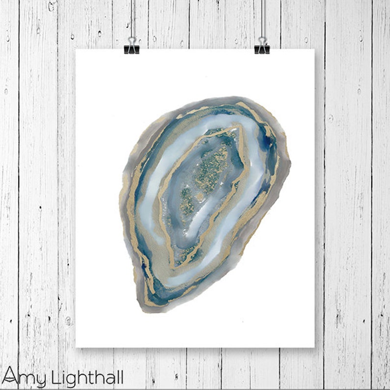 May include: A watercolor print of a geode slice, featuring shades of blue, gray, and gold. The artwork is displayed on a white background and held by two black binder clips. The artist's name, Amy Lighthall, is printed at the bottom.