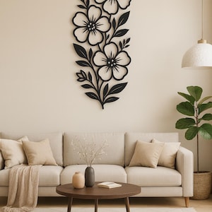 Könnte beinhalten: Schwarze florale Wanddekoration. Dieses dekorative Stück zeigt eine vertikale Anordnung von drei großen Blumen mit detaillierten Blütenblättern und Blättern. Das Kunstwerk ist an einer neutralfarbenen Wand angebracht.