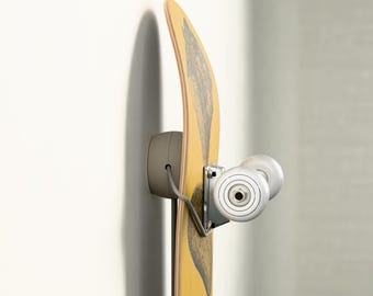 May include: A yellow skateboard with a black graphic design is mounted on a wall. The skateboard is held in place by a gray wall mount and silver hardware. The wheels are white.