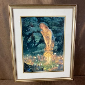 Op de afbeelding: Een ingelijste print van een schilderij met een gloeiende figuur in een donker bos, omringd door kleine, verlichte wezens. Het kunstwerk zit in een metalen gouden lijst met een witte passe-partout en toont een tafereel van licht en schaduw.