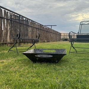 May include: Outdoor seating set with a fire pit. The set includes two black metal chairs with scrolled armrests and a square fire pit with circular cutouts. The chairs and fire pit are on a grassy lawn.