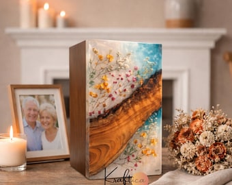May include: A wooden rectangular urn with a resin front panel. The resin panel features a wood grain design with embedded dried flowers in shades of yellow, pink, and white, set against a blue and white background. The urn is displayed with a framed photo and a bouquet.