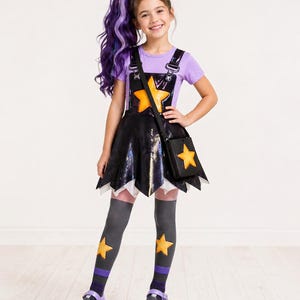 Könnte beinhalten: Ein Kinderkostüm mit einem schwarzen Pailletten-Latzkleid mit einem großen gelben Stern, kombiniert mit einem lila T-Shirt. Das Outfit umfasst eine passende schwarze Handtasche mit einem Stern, graue Kniestrümpfe mit Sternen und lila Schuhe. Eine lila und blaue Perücke vervollständigt den Look.