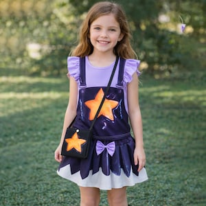 Könnte beinhalten: Ein junges Mädchen trägt ein lila und marineblaues Kleid mit Sternenmotiv und eine passende schwarze Handtasche. Das Kleid hat einen großen orangefarbenen Stern und einen weißen Saum. Die Handtasche hat auch einen orangefarbenen Stern.
