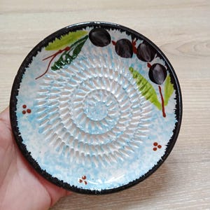 Może przedstawiać: Biały ceramiczny kubek z czarnym uchwytem i napisem "But First, Coffee" pogrubioną, czarną czcionką. Kubek jest umieszczony na neutralnym tle, podkreślając jego prosty design.