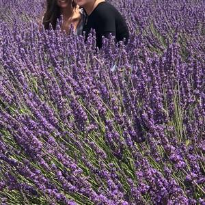 May include: Two people smiling in a field of purple lavender flowers.