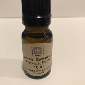 May include: A small brown glass bottle with a black cap, containing lavender essential oil. The label reads "Lavender Essential Oil, Provence, France, 10 ml, www.vintageparismarket.etsy.com, Apex, NC".