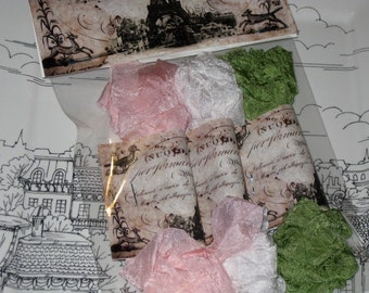 May include: Four rolls of fabric ribbon in pink, white, and green. The ribbon is tied around small, vintage-style paper scrolls with text that reads "N.I.O. performare" and "delicati e rari di Montecitorio e calligrafia".