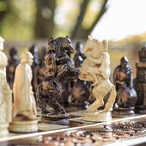May include: A detailed shot of a chess set with intricately carved pieces. The focus is on the knight pieces, one dark brown and one cream-colored, facing each other. The board has a decorative, carved design.
