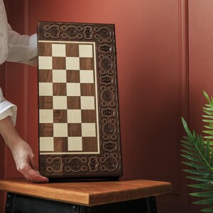 May include: A wooden chess board with a decorative border and a checkered playing surface. The board is brown and cream-colored, with intricate carvings along the edges. The board is rectangular and appears to be handcrafted.