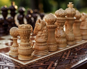 Può includere: Un primo piano di una scacchiera in legno. I pezzi di colore chiaro sono a fuoco, mostrando intagli intricati. La scacchiera ha un motivo a scacchi marrone e crema, con un bordo decorativo. I pezzi più scuri sono sullo sfondo.