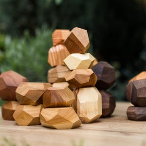 May include: A collection of wooden geometric blocks in various shades of brown and tan. The blocks are stacked and arranged on a wooden surface, showcasing their multifaceted designs. The natural wood tones create a warm, earthy aesthetic.