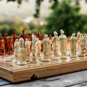 May include: A wooden chess set with intricately carved pieces. The chess board is light brown with a grid pattern. The chess pieces are in two colors: light beige and reddish-brown. The background is blurred with green trees.