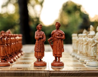 Può includere: Un set di scacchi in legno con pezzi intagliati. I pezzi sono principalmente marroni e color crema, disposti su una scacchiera. L'attenzione è focalizzata sul re e sulla regina, con dettagli sugli abiti e sui volti.