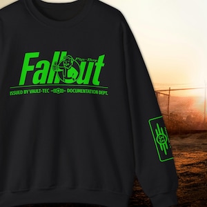 May include: Black sweatshirt with the word "Fallout" in bright green, featuring a Pip-Boy character giving a thumbs up. The text "ISSUED BY VAULT-TEC - DOCUMENTATION DEPT." is below the main graphic. A green graphic is on the sleeve.