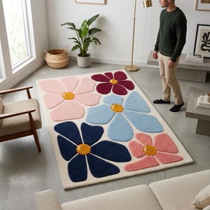 May include: A rectangular area rug featuring a cream-colored background with a large-scale floral pattern. The design includes stylized flowers in shades of light pink, dark blue, light blue, and deep magenta, each with a solid yellow center.