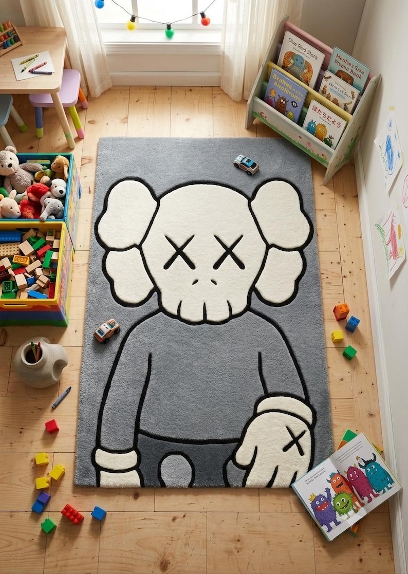 May include: Gray rectangular rug featuring a cartoon character design with white and black accents. The rug is placed on a wooden floor in a child's room, surrounded by toys and a small bookshelf.
