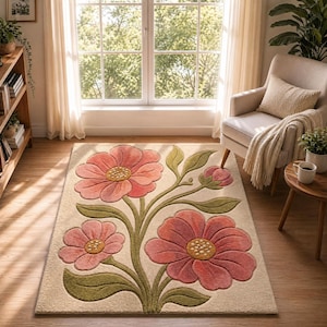 May include: A rectangular area rug with a floral design. The rug features three large pink flowers with yellow centers and green leaves against a beige background. The rug is placed on a hardwood floor in a well-lit room.