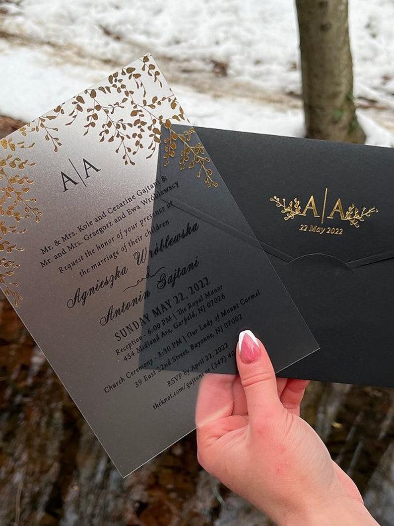 May include: Wedding invitation suite featuring a translucent invitation with gold foil leaf accents and a black envelope. The invitation includes the names Agnieszka and Antonin, the date, and event details. The envelope has the initials "AA" and the date.