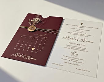 May include: A burgundy wedding invitation set featuring a calendar for August 2024 with a gold heart on the 23rd, a gold wax seal with initials R|R, and dried flowers. Beside it, a white card displays wedding details in black and gold text.