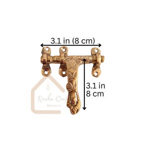 May include: A brass door latch, measuring 8 cm in length and height, with floral and leaf detailing. The latch has a decorative handle and mounting holes. The product is from Racha Craft Morocco.