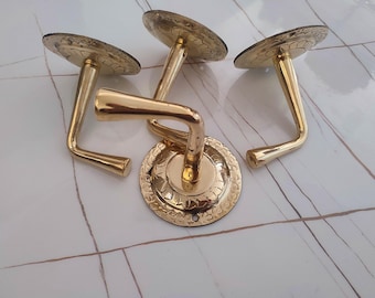 May include: Four gold-coloured cabinet pulls with a decorative floral pattern on the circular base and top. The pulls have a curved handle design, and are made of a shiny, metallic material.