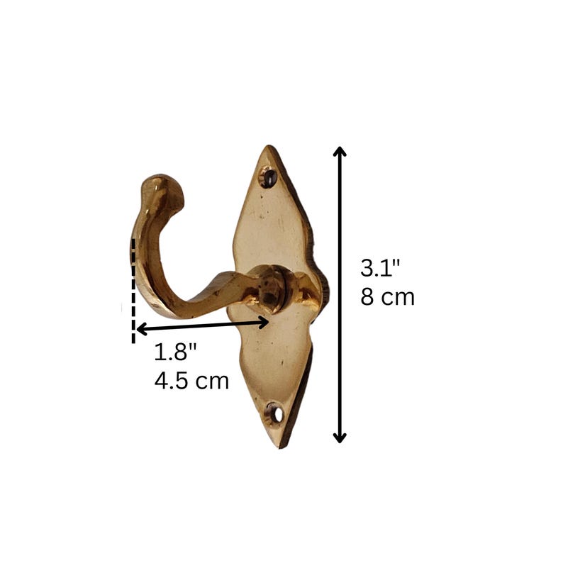 May include: A brass-colored wall hook with a decorative diamond-shaped backplate. The hook is 1.8 inches (4.5 cm) wide and 3.1 inches (8 cm) tall. It has a curved hook design and two screw holes for mounting. The hook is made of metal.