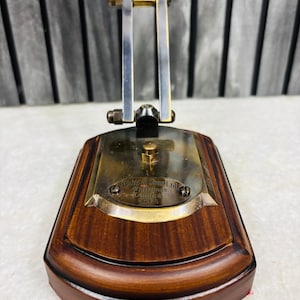 May include: A vintage brass and wood desk lamp with a rectangular base. The base is made of dark wood with a curved edge. The lamp has a brass plate with the text "W & S Sons Ltd Opticians London 1614". The lamp's frame is made of metal.