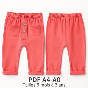 May include: Coral-colored baby pants with a buttoned front and two front pockets. The pants have a comfortable elastic waistband and cuffed hems. The text "PDF A4-A0 Tailles 6 mois à 3 ans" is printed at the bottom of the image.