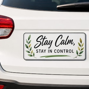 以下が含まれることがあります： Stay Calm, STAY IN CONTROLという黒い文字が書かれた長方形の白い車用マグネット。左右には水彩画風の緑の葉の枝が描かれており、テキストの下には緑色の水平なブラシストロークのアクセントが施されています。