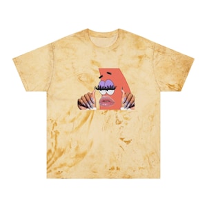 May include: A unisex t-shirt with a unique design. The shirt has a marbled, tan and yellow pattern. The graphic features a cartoon character with long eyelashes, glossy lips, and manicured nails. The shirt is a casual wear item.