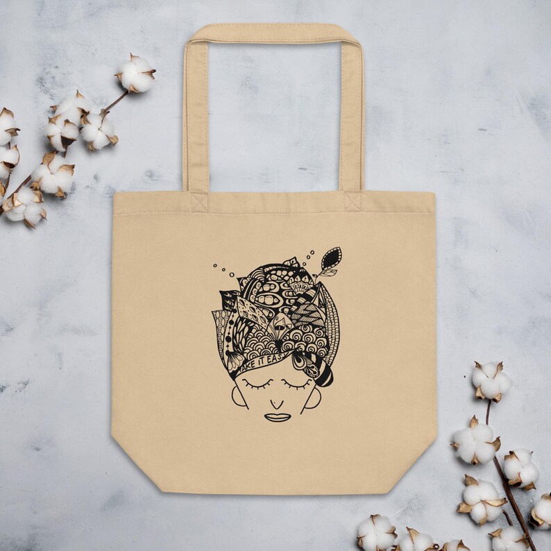 Peut inclure: Sac fourre-tout beige avec une illustration en noir et blanc d'un visage aux yeux ferm&eacute;s et d'un motif de t&ecirc;te d&eacute;taill&eacute;. Le texte "MAKE IT EASY" est visible. Le sac a deux anses et est fait d'un mat&eacute;riau semblable &agrave; de la toile.