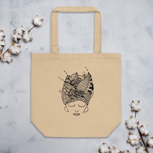 Pu&ograve; includere: Borsa tote beige con un'illustrazione in bianco e nero di un volto con gli occhi chiusi e un'acconciatura dettagliata. L'acconciatura &egrave; piena di vari motivi e forme. La borsa ha due manici ed &egrave; realizzata in tela.