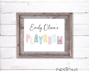 May include: A framed sign with the text "Emily Olivia's Playroom" in colorful letters. The letters are outlined in black and have a white background. The frame is made of weathered wood.