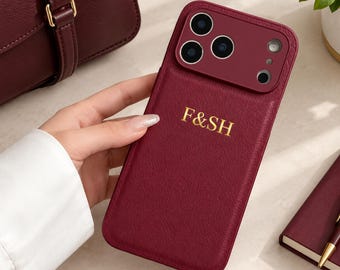 May include: A burgundy leather phone case featuring a camera cutout and the gold embossed letters F&SH. The case has a textured finish and a matching burgundy camera lens frame, providing a sleek look for a mobile device.