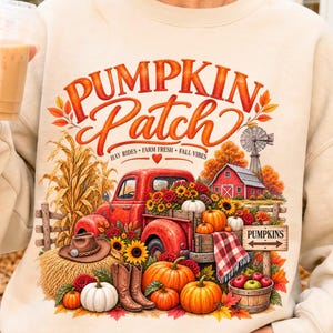 May include: A beige crewneck sweatshirt featuring a graphic print of a red pickup truck loaded with pumpkins and sunflowers. The text reads PUMPKIN Patch, HAY RIDES, FARM FRESH, FALL VIBES, and PUMPKINS. The scene includes a barn, windmill, and boots.