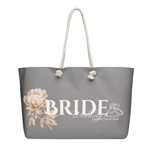 May include: A gray tote bag with white rope handles. The bag features the word "BRIDE" in large white letters, a floral design, and the text "Wedding muse J SMITH COLLECTION".