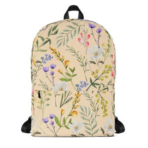 Puede incluir: Una mochila beige con un estampado floral con flores blancas, moradas, amarillas y rosas, y hojas verdes. La mochila tiene correas negras y un asa negra. El diseño es de estilo acuarela.