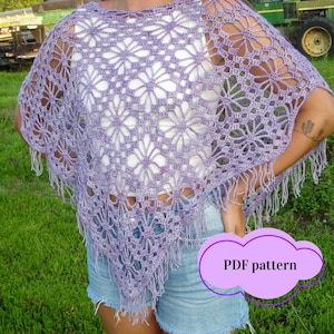 May include: A lavender crochet poncho with a floral pattern and fringe trim. The poncho is open-weave, revealing the garment underneath. The image includes the text "PDF pattern" in a purple cloud-shaped graphic. The poncho is worn over a white top and denim shorts.