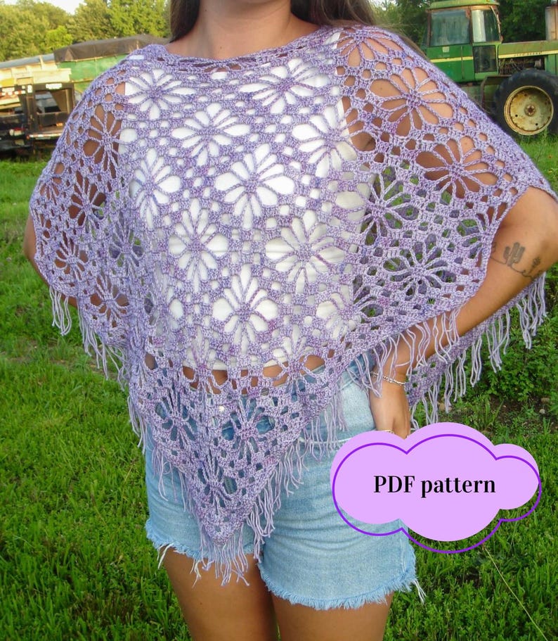 May include: A lavender crochet poncho with a floral design and fringed edges. The open-weave design reveals the clothing beneath. The image includes the text "PDF pattern" in a purple cloud-shaped graphic. The poncho is worn over a white top and denim shorts.
