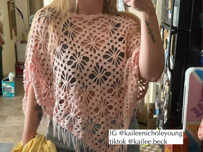 May include: A light pink crochet poncho with a floral design. The poncho has a fringed hemline and is made of a soft, open-weave material. The image includes the text "IG @kaileenicholeyoung tiktok @kailee.beck".