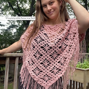 May include: A light pink crochet poncho with a floral pattern and fringe. The poncho is handmade and features a V-neck design. The text "@sunnystitchescrochet" is visible in the image. This item is perfect for adding a touch of bohemian style to any outfit.