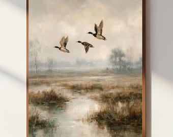 Op de afbeelding: Een ingelijst landschapsschilderij met drie eenden die over een moeras vliegen. Het kunstwerk gebruikt gedempte tinten bruin, grijs en beige, met de nadruk op de vogels en de mistige omgeving. Het schilderij is ingekaderd in een bruine houten lijst.