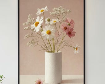 Op de afbeelding: Een ingelijste print met een bloemstuk. Witte madeliefjes met gele centra en roze cosmosbloemen staan in een witte cilindervormige vaas. De achtergrond is zachtroze en er ligt een enkele roze bloem op het oppervlak.