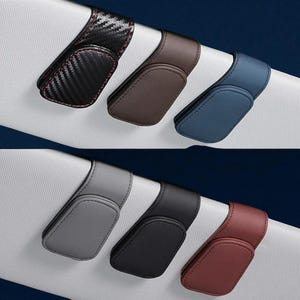 Puede incluir: Una colección de soportes para clips de visera de coche en varios colores. Los soportes son de fibra de carbono negra, marrón, azul, gris, negro y burdeos. Cada clip tiene un diseño curvo y una pequeña almohadilla rectangular.