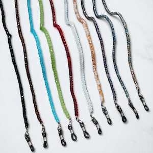 Könnte beinhalten: Eine Sammlung von Brillenketten mit Perlen in verschiedenen Farben, darunter Schwarz, Braun, Türkis, Grün, Rot, Weiß, Orange, Lila und Blau. Jede Kette hat eine Schlaufe zum Befestigen an Brillen.