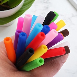 May include: A collection of colorful silicone pen or pencil grips in various shades, including orange, pink, blue, red, yellow, green, black, and brown. The grips are cylindrical with a hole at one end.